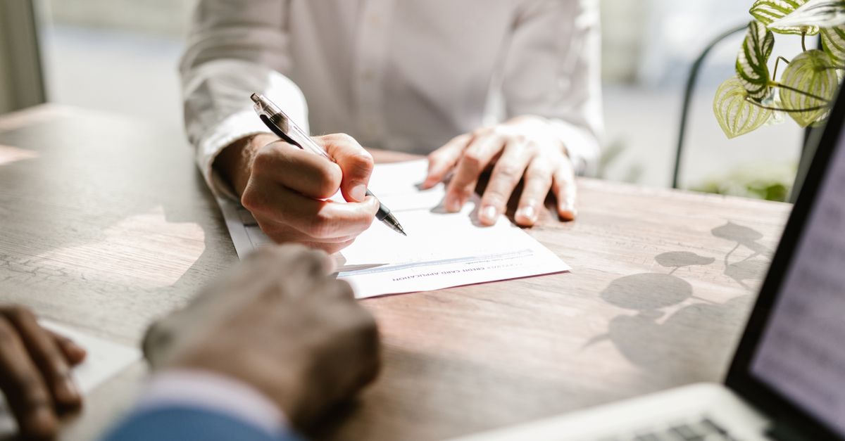 Close-up of people signing a document at a desk, highlighting professional business interaction.