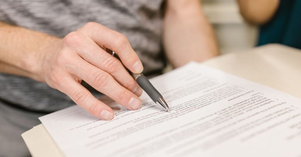Close-up of a person's hand signing an important legal document with a pen indoors.