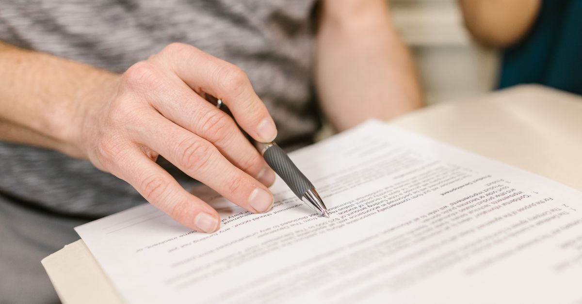 Close-up of a person's hand signing an important legal document with a pen indoors.