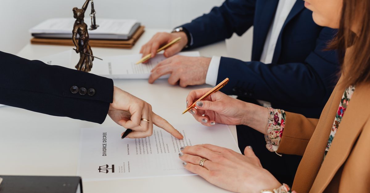 Hands signing a divorce decree, with a justice statue nearby, symbolizing legal proceedings.