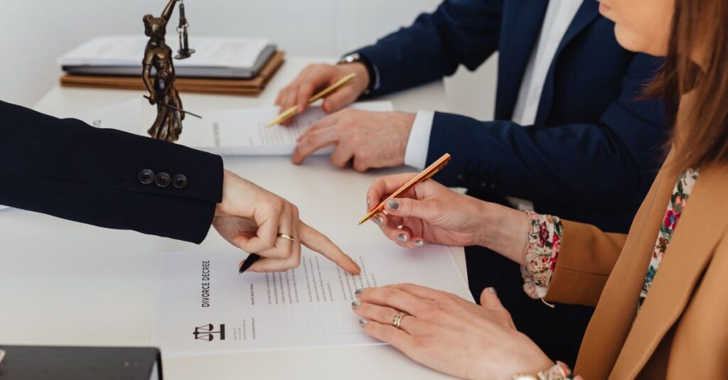 Hands signing a divorce decree, with a justice statue nearby, symbolizing legal proceedings.