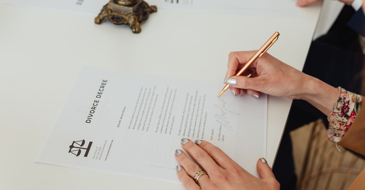Close-up of hands signing a divorce decree document on a desk, showcasing legal process.
