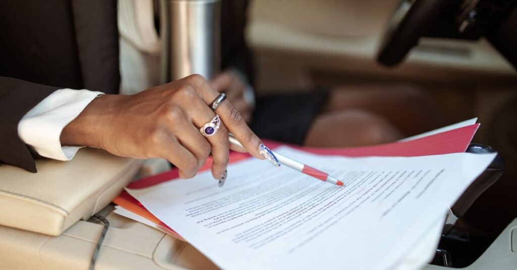 A professional reviewing documents in a car interior, focusing on hand and paperwork.