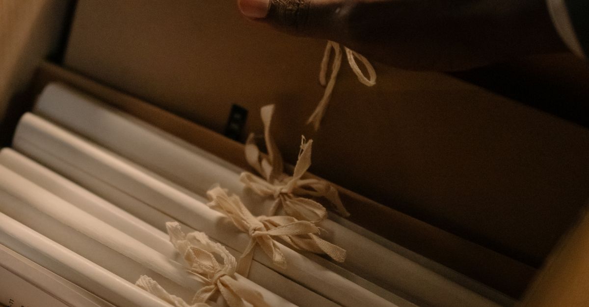 A hand reaches for tied documents inside an archive box, suggesting investigation or record keeping.