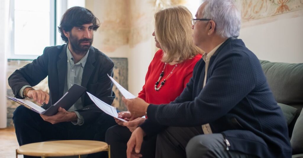 An advisor discussing financial documents with a senior couple indoors in a cozy living room setting.