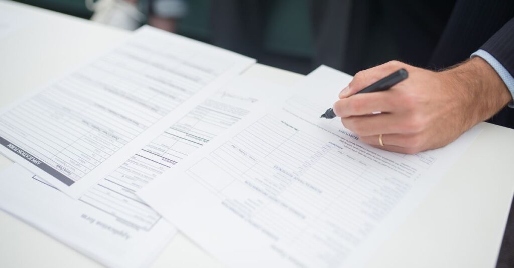 Close-up of a hand signing insurance documents in an office setting.