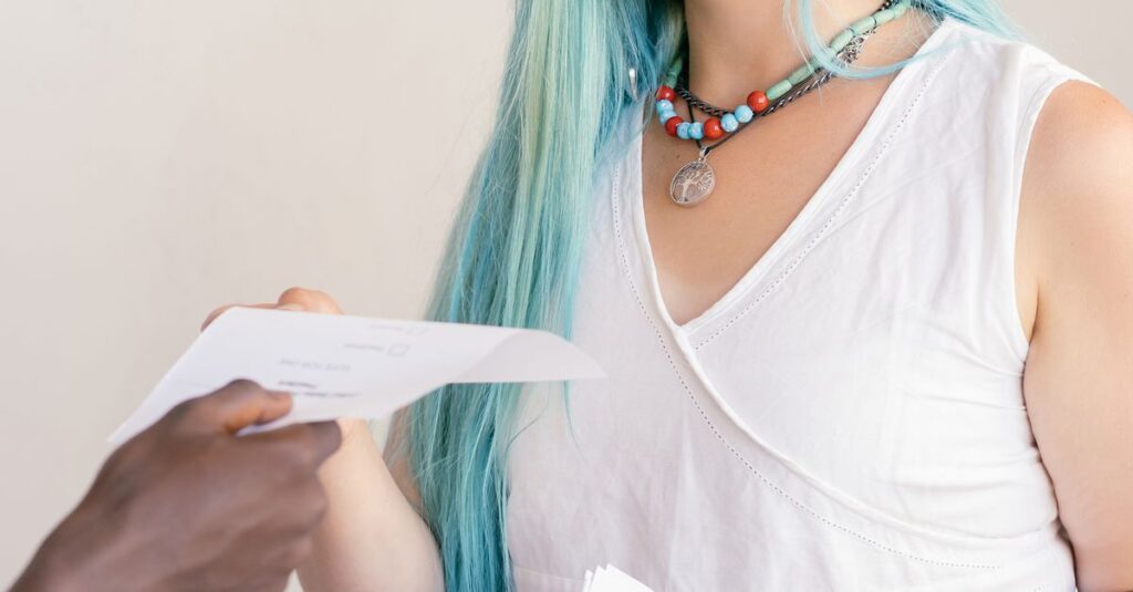 Smiling woman with blue hair handing a paper to another person indoors.