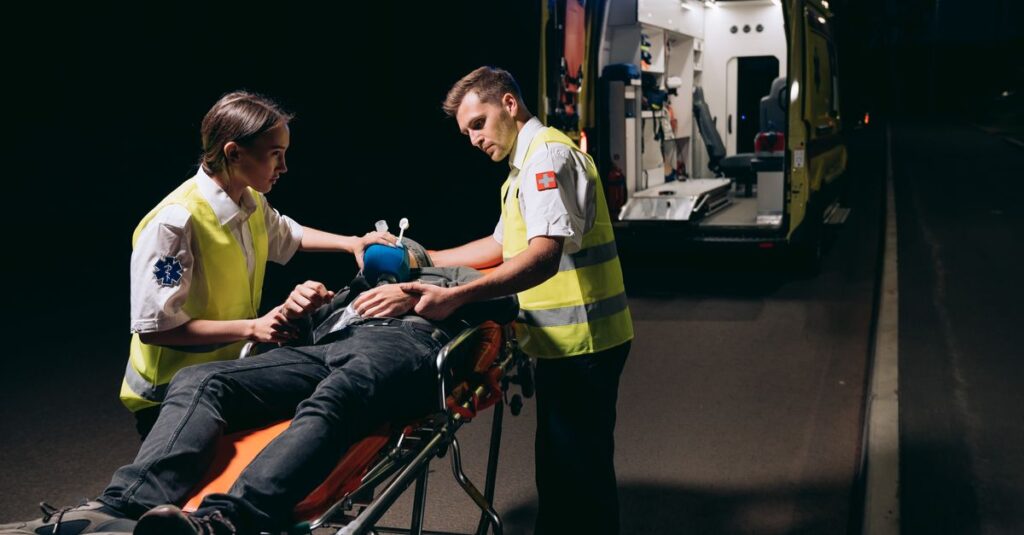 Paramedics attending to a patient on a stretcher with an ambulance nearby at night.