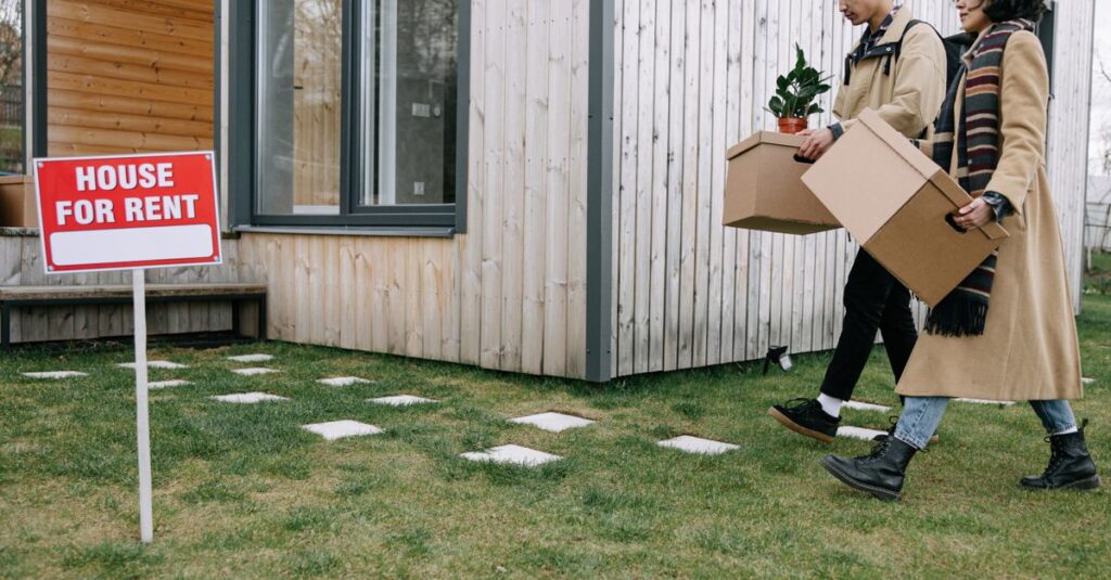 Young couple carrying boxes into their newly rented house, symbolizing new beginnings.