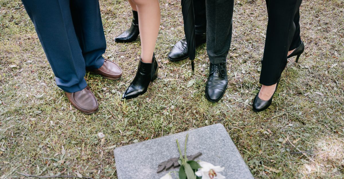 Shoes of mourners gathered around a gravestone with lilies in a cemetery.