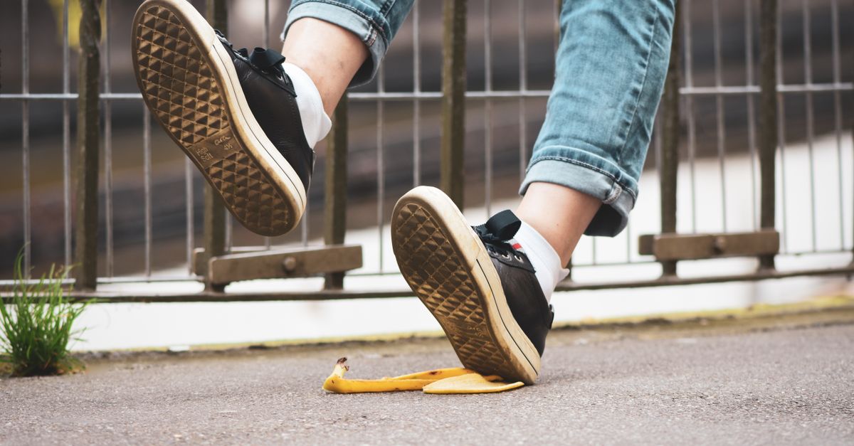 Close-up of a person slipping on a banana peel, wearing sneakers and jeans on a street.