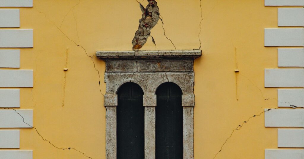 Close-up of a weathered yellow building façade with cracks, featuring arched windows and shutters.