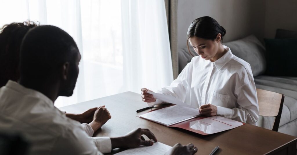 A professional woman reviews documents with a couple at home, indicating a collaborative decision-making process.