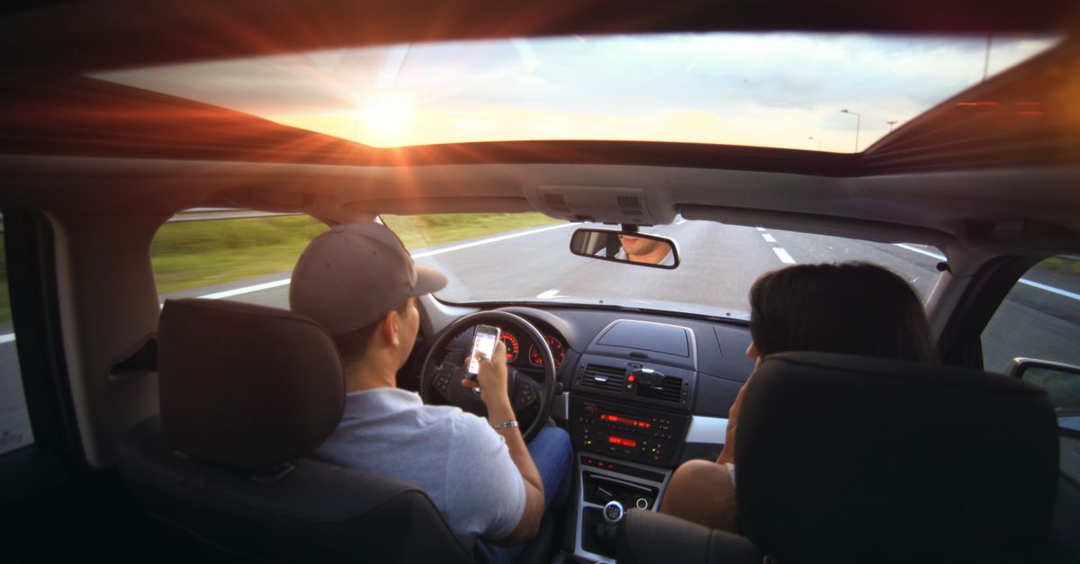 Driver using phone while driving at sunset with passenger in vehicle.