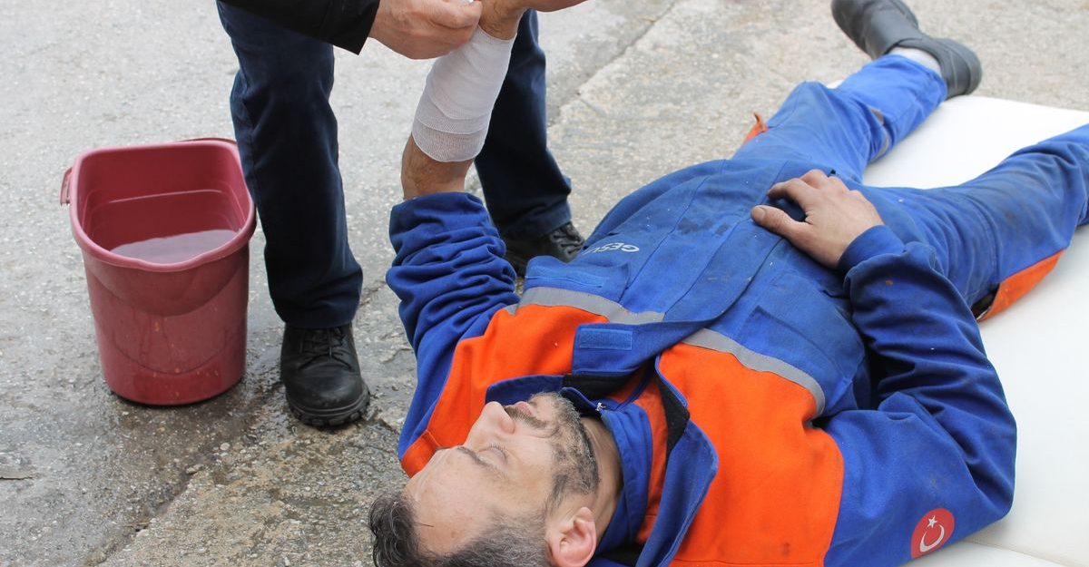 Injured worker receiving first aid on-site with arm bandage applied.