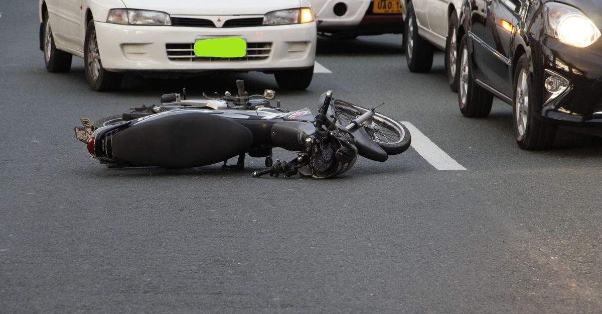 A motorcycle lies on a city road amidst traffic, indicating a recent accident.