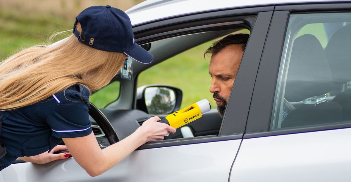 Police officer using breathalyzer to test driver's alcohol level outside car.