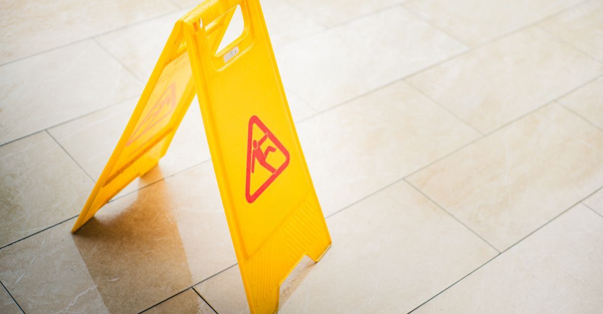 A bright yellow caution sign on a tiled floor indicates a wet surface, alerting passersby to potential hazards.