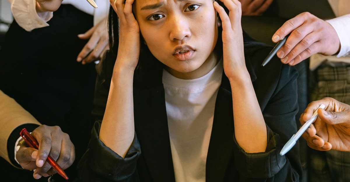 Stressed Asian businesswoman surrounded by demanding colleagues in a busy office setting.