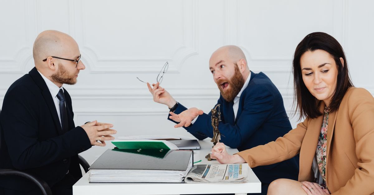 A heated discussion between two men and a woman in a corporate office setting.