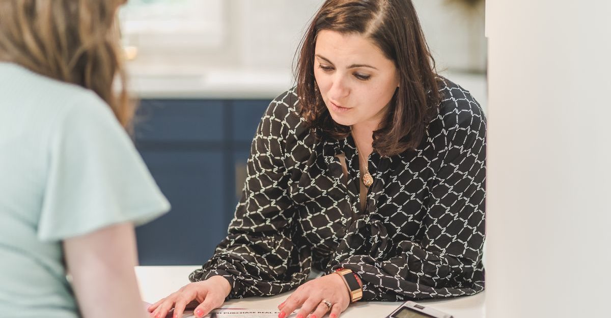 Real estate agent discussing paperwork with a client in a bright, modern office setting.