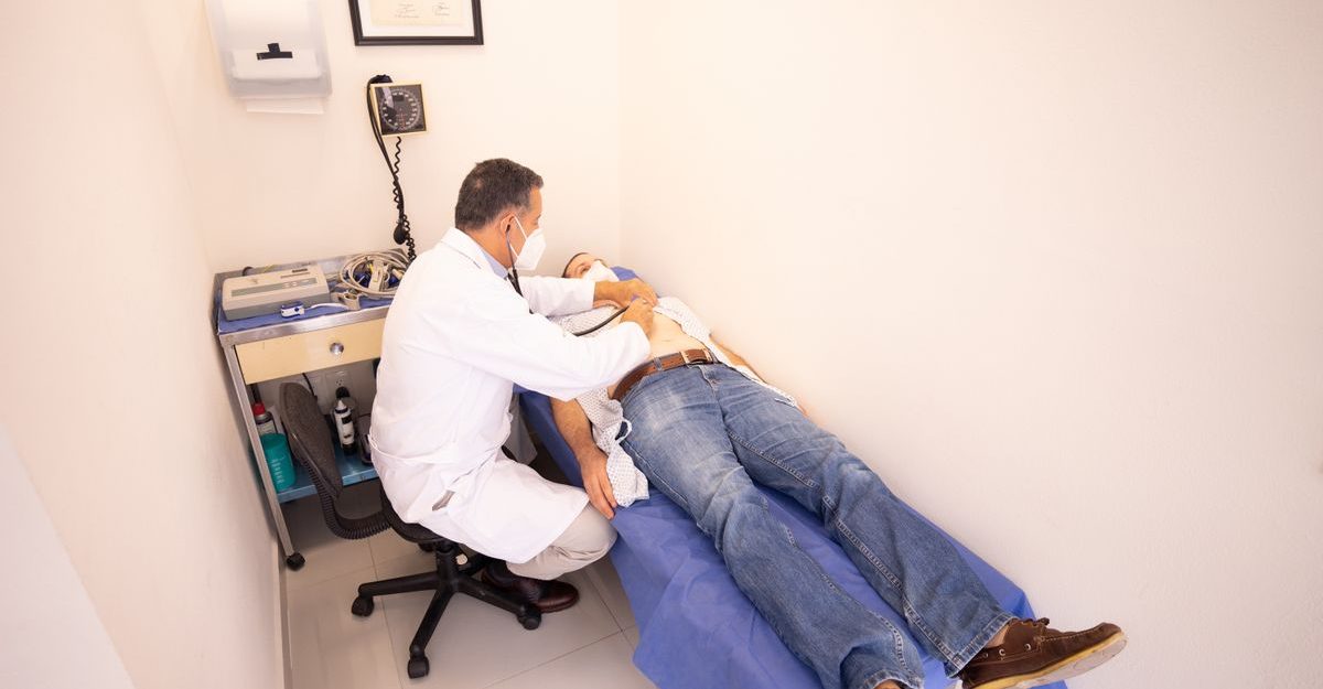 Medical professional examines patient with stethoscope in clinic examination room.