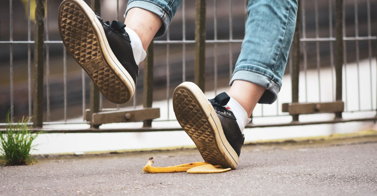 Close-up of a person slipping on a banana peel, wearing sneakers and jeans on a street.